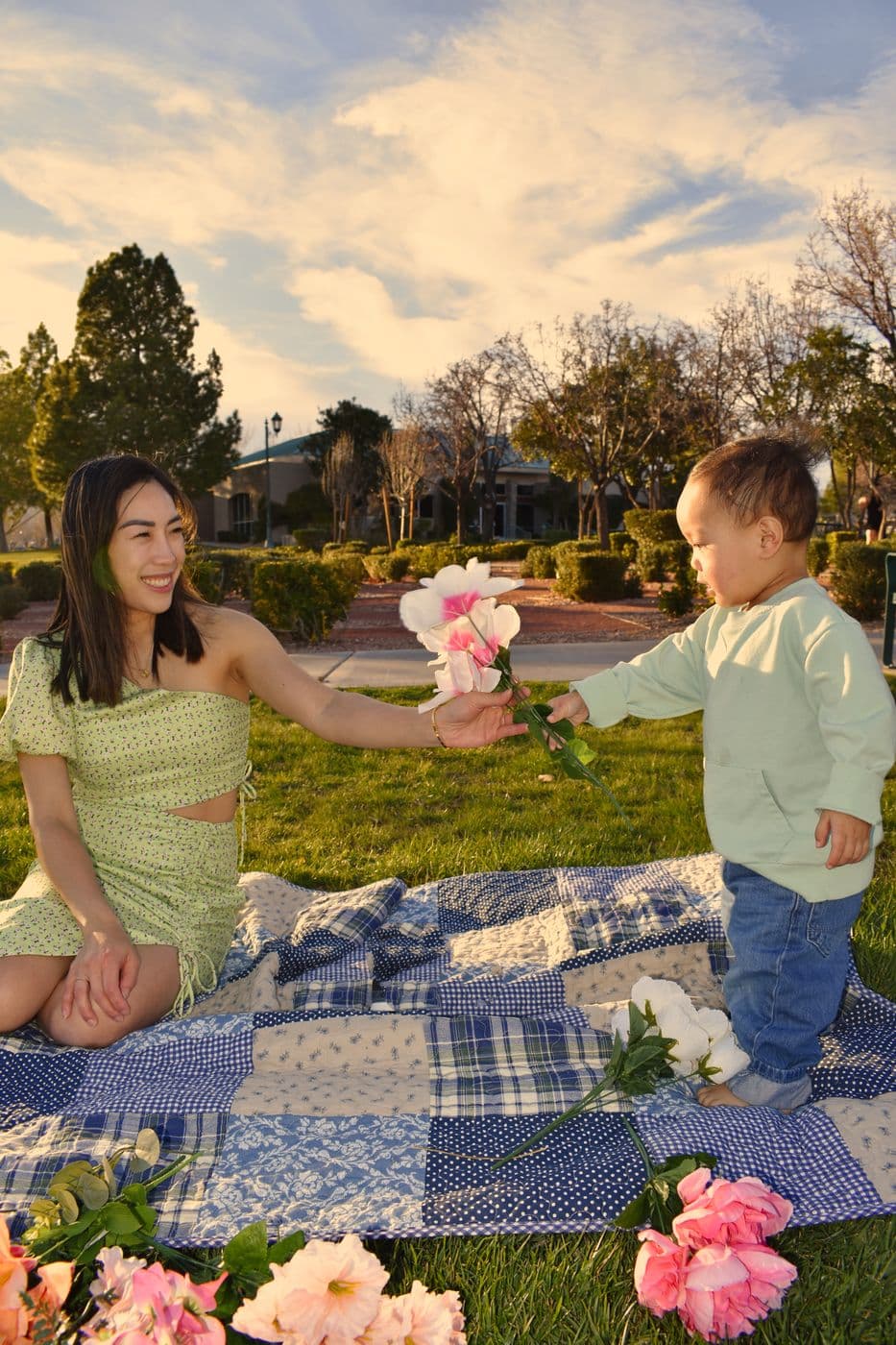 A mother on a quilted picnic blanket handing flowers to her toddler at a Las Vegas park during golden hour