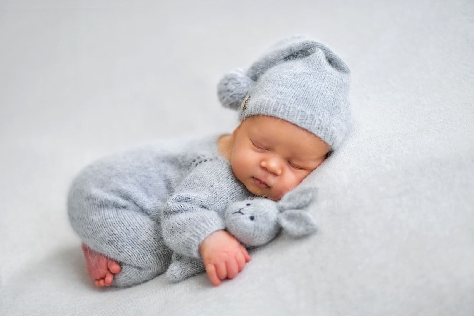 A sleeping newborn in a soft blue knit romper and sleepy cap curled on a white blanket during an in-studio newborn session in Las Vegas, NV